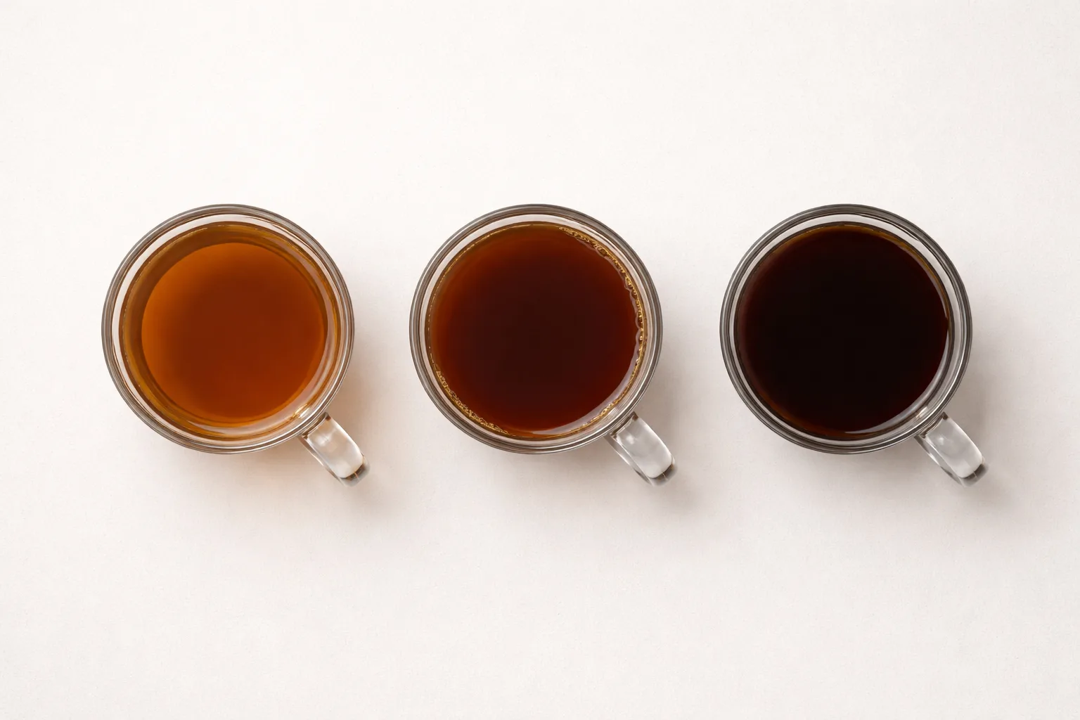 Üstten çekimde üç cam kupada solda berrak, ortada orta, sağda koyu kahve